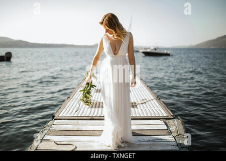 Giovane sposa in abito da sposa in piedi sul lago pier, Stresa, Piemonte, Italia Foto Stock