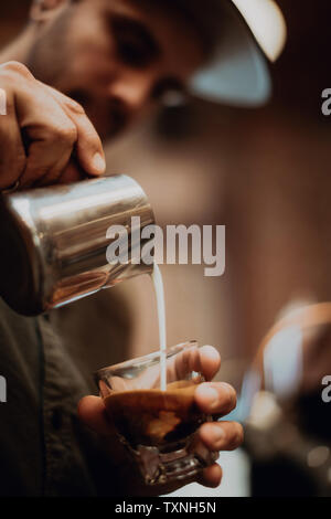 Barista versando il latte nel caffè di vetro in cafe, close up delle mani Foto Stock