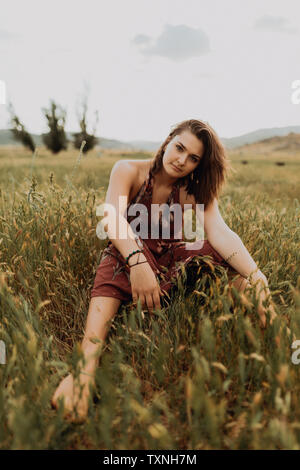 Bella giovane donna seduta nel campo di erba lunga, ritratto, Exeter, CALIFORNIA, STATI UNITI D'AMERICA Foto Stock