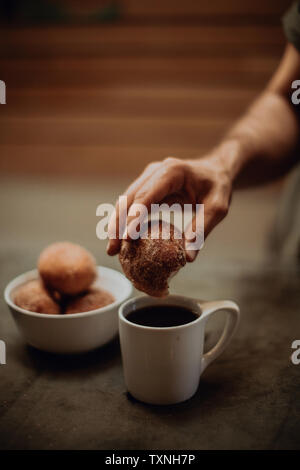 Uomo ciambella di immersione in nero caffè al tavolo, ritagliata messa a fuoco poco profonda Foto Stock