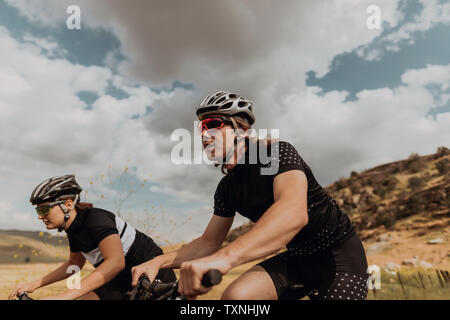 Giovane coppia di Ciclismo Ciclismo su strada rurale, vista laterale, Exeter, CALIFORNIA, STATI UNITI D'AMERICA Foto Stock