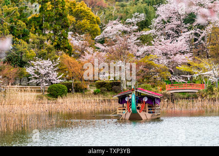 Kyoto, Giappone - 11 Aprile 2019: fiore di ciliegio da Osawa-no-ike stagno lago in primavera in area Arashiyama dal Tempio Daikakuji con rosso tradizionale tour boa Foto Stock