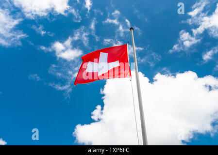 Sventolare nel vento a sinistra la bandiera della Svizzera appeso sul montante, contro lo sfondo del cielo blu con nuvole bianche. Foto Stock