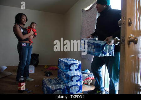 Kiara Smith, tenendo il suo nipote Joshua Byrd, 7 mesi, orologi come volontario offre casi di acqua in bottiglia all'Evergreen Regency Apartments di Flint, Michigan, 5 marzo 2016. La selce residenti continuano a usare acqua in bottiglia dopo l'acqua potabile è stata trovata essere contaminato con piombo dopo la fonte di acqua è stato commutato da Detroit acqua e la rete fognaria Dipartimento per il fiume Flint in aprile, 2014. Foto di Molly Riley/UPI Foto Stock