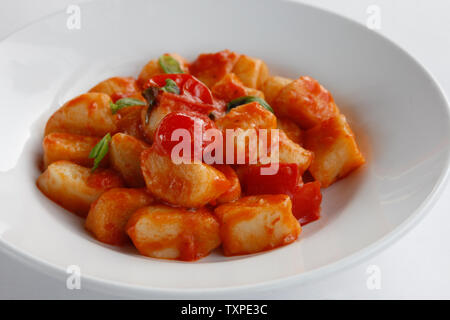 Close up di gnocchi con pomodorini e basilico isolato su una piastra bianca e sfondo bianco Foto Stock