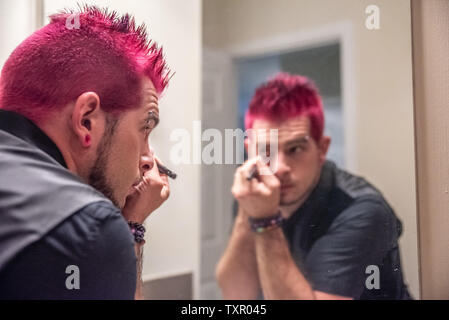 Diversi caucasici uomo maschio con dentato per capelli rosa applicazione eyeliner specchio dello specchio di riflessione. Indossa abiti neri con punk rocker l alternativa Foto Stock