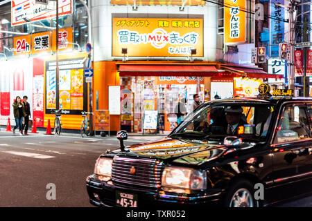 Osaka, Giappone - 13 Aprile 2019: Minami Namba street con edifici illuminati segni colorati e nero con taxi nel traffico Foto Stock