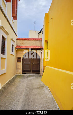 Piccola strada che conduce verso i cancelli di colore marrone con una parete gialla su un lato e uno marrone a muro di pietra sul lato opposto Foto Stock