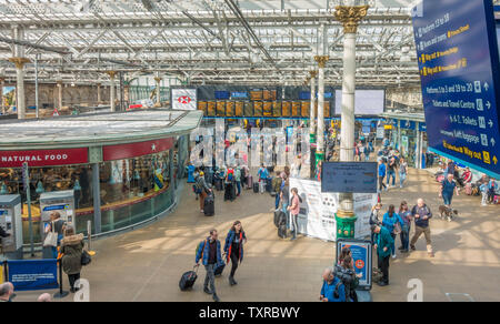 Scena in interni di un occupato la stazione ferroviaria Waverley di Edimburgo, con la luce del sole lo streaming attraverso il vetro e il tetto di travi. La Scozia, Regno Unito. Foto Stock