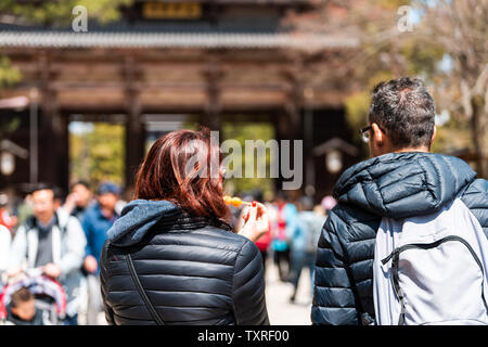 Nara, Giappone - 14 Aprile 2019: turisti giovane torna closeup di persone al Tempio Todaji in città durante il giorno da gate di mangiare dango Foto Stock