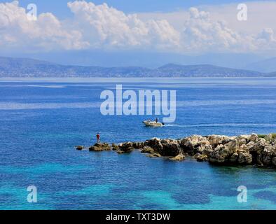 Un uomo la pesca da alcune rocce a Kassiopi,Kassopaia,Isole Ionie, Corfù ,Grecia Foto Stock