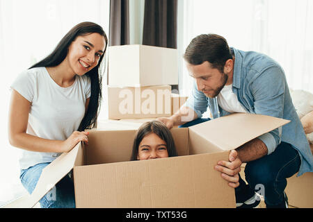 La famiglia felice avendo divertimento mentre si sposta in un nuovo appartamento. Madre, padre e figlia insieme sorridente, con le scatole di cartone su sfondo Foto Stock