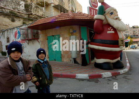 Ragazzi palestinesi sostare nelle vicinanze di un gonfiabile gigante Santa Claus presso un negozio di biblico della Cisgiordania città di Betlemme dove i cristiani credono che Gesù era nato, Dicembre 16, 2004. Tradizionali decorazioni di Natale non saranno visualizzati in Betlemme fino a quando i quaranta giorni di lutto per il defunto leader palestinese Yasser Arafat termina pochi giorni prima di Natale. (UPI foto/Debbie Hill) Foto Stock