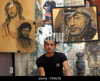 Un uomo palestinese si siede di fronte a disegni di Gesù Cristo, il leader degli Hezbollah Hassan Nasrallah e alla fine il leader palestinese Yasser Arafat in una strada a Ramallah in Cisgiordania, 10 settembre 2006. (UPI foto/Debbie Hill) Foto Stock