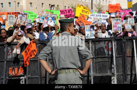 Un israeliano funzionario di polizia si erge vicino come israeliani etiope tenere le foto di parenti ancora in Etiopia a una dimostrazione al di fuori del Primo Ministro israeliano Benjamin Netanyahu dell'ufficio in Gerusalemme, 10 gennaio 2009. I manifestanti hanno chiesto al governo di fine della politica di discriminazione contro la concessione di immigrazione di ebrei etiopi. Ci sono alcuni 8.700 ebrei etiopi ancora in attesa di immigrare in Israele . UPI/Debbie Hill Foto Stock