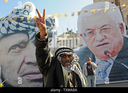 Un uomo palestinese lampeggia il segno della vittoria di fronte a grandi blow-up ritratti della fine del leader palestinese Yasser Arafat e il presidente palestinese Mahmoud Abbas in un rally che celebra il 46° anniversario del movimento Fatah a Ramallah in Cisgiordania, 3 gennaio 2011. UPI/Debbie Hill Foto Stock