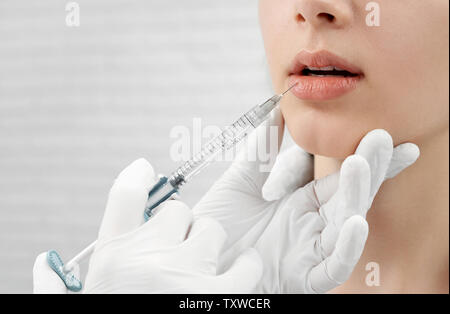 Close up di mani in gomma bianca guanti medicali rendendo iniezione, tenendo la siringa, toccando mento femmina. Ben curato volto di giovane donna la ricezione di botox di labbra. Concetto di bellezza. Foto Stock