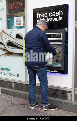 L'uomo riceve denaro al di fuori di un ATM / punto di contanti al di fuori di un negozio Costcutter a Stirling, Scozia, Regno Unito Foto Stock