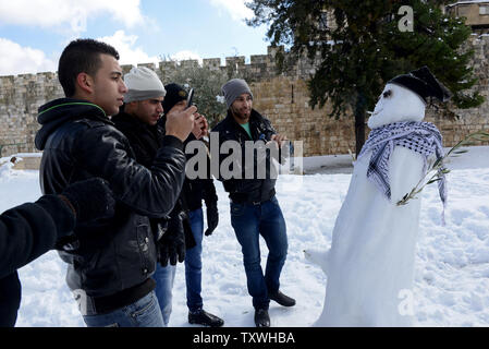 Palestinesi di scattare delle foto di un pupazzo di neve al di fuori delle mura della Città Vecchia di Gerusalemme, Israele, Dicembre 13, 2013. Un inizio di grande tempesta di neve ha coperto le parti del Medio Oriente con neve pesante, causando interruzioni di elettricità e la chiusura delle scuole e le strade di Gerusalemme. UPI/Debbie Hill Foto Stock