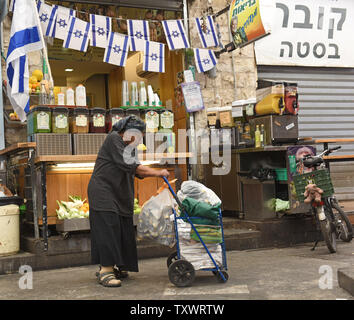 Una donna anziana spinge un carrello di lattine di lattina passato una linea di piccolo israeliano bandiere nazionali appeso in onore di Israele il giorno della memoria per i caduti e le vittime del terrore e indipendenza giorni a Gerusalemme, Israele , 10 maggio 2016. Un minuto di sirena suona il martedì sera per iniziare a Israele il giorno memoriale per i soldati e civili vittime del terrore. Israele potrà commemorare 23,447 soldati IDF e terrore vittime uccise dal 1860. Cerimonie ufficiali si terrà presso i cimiteri militari di tutto Israele il mercoledì mattina ed il paese è in lutto si rivolgerà a festeggiamenti quando Israele la 68a Foto Stock