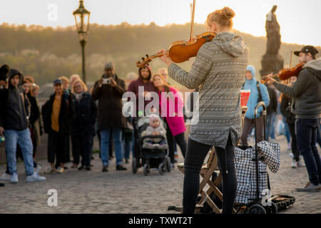 Praga, Repubblica Ceca - 10 APRILE 2019: Una donna musicista e la sua band suona per i turisti con il famoso Ponte Carlo a Praga durante una bassa al tramonto. Foto Stock