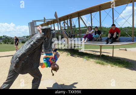 Una famiglia gioca sulla scultura chiamato "dicembre 17, 1903' come esso si replica la scena del primo volo dei fratelli Wright a Wright Brothers National Memorial in uccidere diavolo sulle colline vicino a Kitty Hawk sul Outer Banks della Carolina del Nord il 25 luglio 2015. La ragazza è montata oscillante sul braccio di Wilbur che stava spingendo il piano prima del decollo. La scultura raffigurante Orville a bordo pesa 10.000 libbre, considerando che i fratelli Wright piano "Flyer 1' pesato 605 libbre. Il piano originale è presso lo Smithsonian di Washington DC. Orville e Wilbur Wright ha fatto le loro prove di parapendio dal 1900 e fl Foto Stock