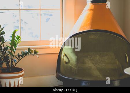 Camino arancione moderno in una sala minimalista con grandi vetrate finestra e una pianta Foto Stock