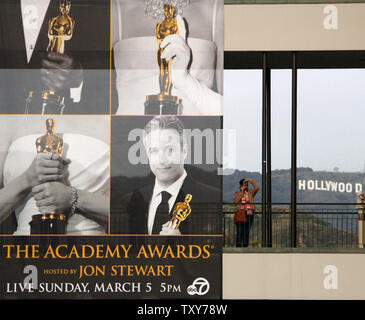 Un visitatore scatta una foto di fronte alla famosa Hollywood Sign come essa si erge accanto a un banner per gli Academy Awards con host Jon Stewart nella sezione di Hollywood di Los Angeles il 3 marzo 2006. Oscar sono programmati per essere consegnati di domenica. (UPI foto/Jim Ruymen Foto Stock