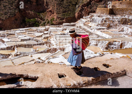 Locale Donna Peruviana a piedi su Salineras de Maras / Maras Miniere di Sale. Estrazione del sale a Maras saline, terrazze e stagni, Perù Valle Sacra. Foto Stock