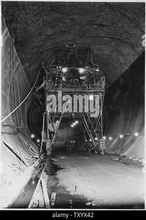 Pistola di calcestruzzo carrello utilizzato in immissione 110 grado top-arch concreta nel tunnel di diversione, campo di applicazione e il contenuto: fotografia dal volume due di una serie di album di foto per documentare la costruzione della Diga di Hoover, Boulder City, Nevada. Didascalia completa delle fotografie si legge: Calcestruzzo gun carrello utilizzato in immissione 110 grado top-arch concreta nel tunnel di diversione. Il calcestruzzo viene trasportata dal carrello in discarica-secchi in posizione sotto il carrello, issato al ponte superiore mediante gru a ponte overhead operativi, oggetto di dumping nelle tramogge e costretti in forma mediante aria compressa attraverso due 8 pollici di acciaio e tubi di gomma. Due Foto Stock