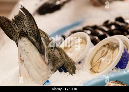 Un salmone fresco e somepackeged prodotti in vendita mostrando una coda bloccata in una bocca del pesce alla Granville Island il mercato pubblico, Vancouver, Canada. Foto Stock