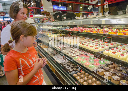 La ragazza e sua madre per prendere il loro tempo a guardare alla varietà di colorate torte offerto al Granville Mercato Pubblico, Vancouver, Canada. Foto Stock