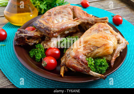 Tutto il coniglio al forno con i verdi e i pomodori su una piastra. Gustosa carne dietetici. Foto Stock