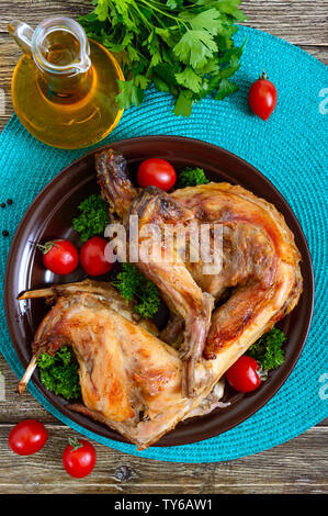 Tutto il coniglio al forno con i verdi e i pomodori su una piastra. Gustosa carne dietetici. Foto Stock