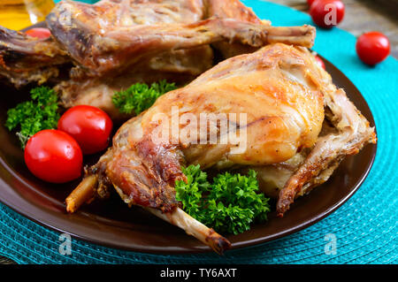 Tutto il coniglio al forno con i verdi e i pomodori su una piastra. Gustosa carne dietetici. Foto Stock