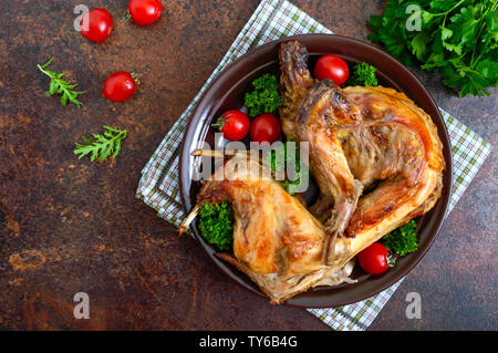 Tutto il coniglio al forno con i verdi e i pomodori su una piastra. Gustosa carne dietetici. Vista superiore, piatto laici. Foto Stock