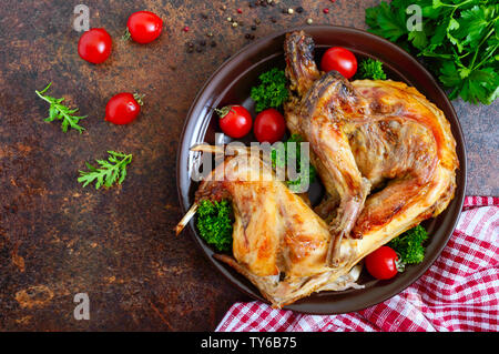 Tutto il coniglio al forno con i verdi e i pomodori su una piastra. Gustosa carne dietetici. Vista superiore, piatto laici. Foto Stock