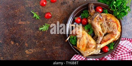 Tutto il coniglio al forno con i verdi e i pomodori su una piastra. Gustosa carne dietetici. Vista superiore, piatto laici. Banner Foto Stock