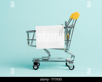 Carrello spesa e white paper nota elenco su sfondo blu. Il concetto di shopping su sfondo blu. Vuoto di carta bianca nota su carrello. Copia spazio per il testo o il design. Foto Stock