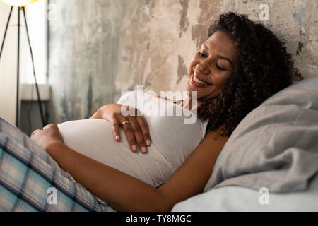 Bella sorridente donna incinta toccando il suo ventre. Foto Stock