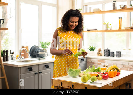 Donna incinta rendendo insalata nella sua cucina. Foto Stock