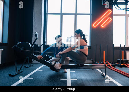 Il Trainer assiste donna con lieve sovrappeso in palestra Foto Stock