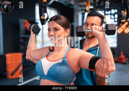 Trainer aiutando donna positivo facendo esercizi per i bracci Foto Stock