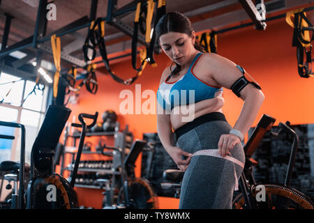 Paffuto donna in grigio leggings misurando le cosce prima di allenamento Foto Stock