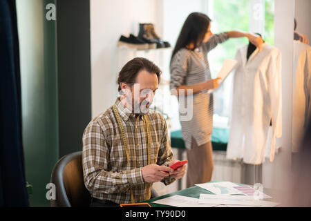 Attraente bello bello dai capelli scuri designer per adulti facendo clic sul telefono Foto Stock