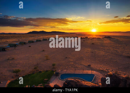 Il tramonto sopra i piccoli chalets di una desert lodge vicino al Sossusvlei in Namibia Foto Stock