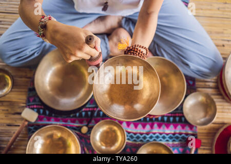 Donna che gioca su Tibetan Singing Bowl mentre è seduto sul materassino yoga contro una cascata. Tonned vintage. Bellissima ragazza con perle di mala meditando Foto Stock