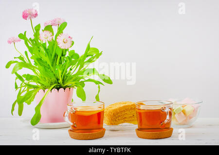 Due tazze di tè nero, marshmallows, fette di torta e un fiore rosa vaso sul tavolo, con spazio di copia Foto Stock