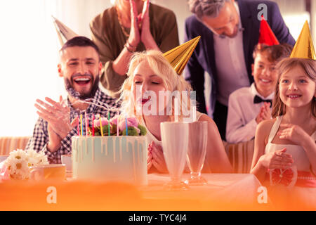 Donna bionda con capelli ondulati soffiando candele sulla torta di compleanno Foto Stock