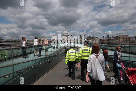 I funzionari di polizia sul Millennium bridge si mescolano con i membri del pubblico nei pressi del luogo in cui la notte scorsa tre terroristi ha ucciso sette persone e il ferimento di 48 dopo aver guidato un furgone a pedoni e commettendo un coltello delirante atack nel vicino mercato di Borough, 04 giugno 2017. La polizia forensics ufficiali continuano a cercare prove nella zona e grandi parti di Londra rimane bloccato su OFF. UPI foto/Hugo Philpott Foto Stock